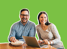 smiling couple sitting at the table looking at their laptop