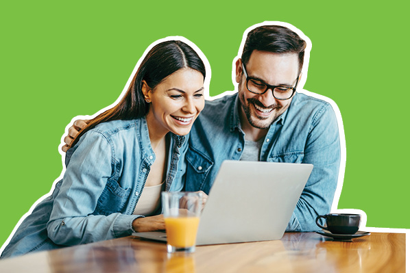 smiling couple sitting at the table looking at their laptop