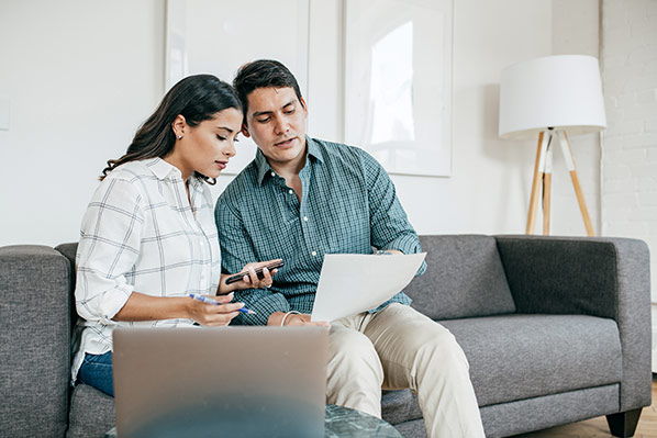 a couple sitting on their living room couch looking at their laptop talking