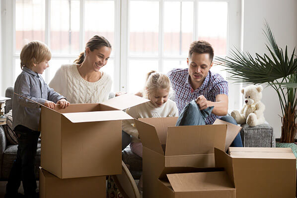 parents with a young daughter and a young son unpacking moving boxes in their new living room