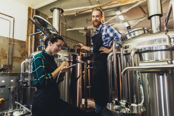 A man and a woman working at work surrounded by large vats