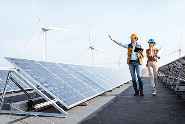 A man and a woman walking solar panels with wind turbines in the background