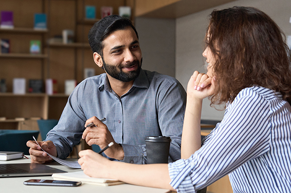 A couple sitting at a table, reviewing paperwork and smiling at each other.