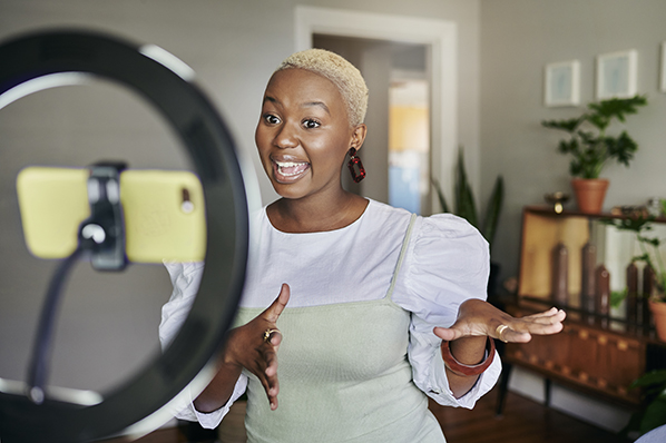 Young woman doing a dance in living room in front of a cell phone mounted in a ring light.