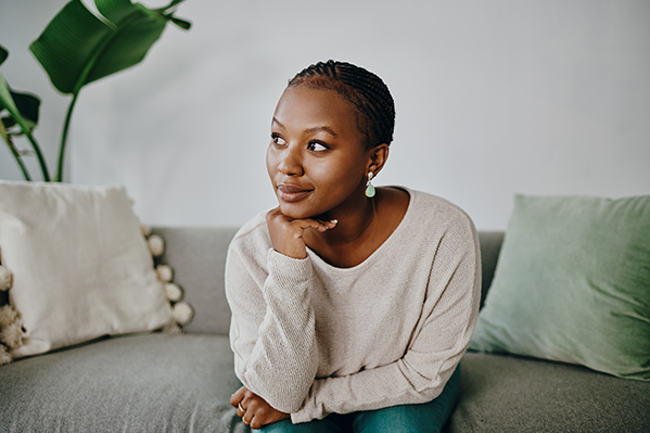 Young woman wearing white sweater sits on couch.