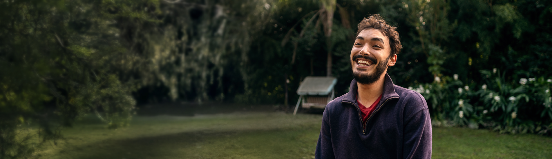A young man with short hair and a beard wearing a purple sweater smiling big