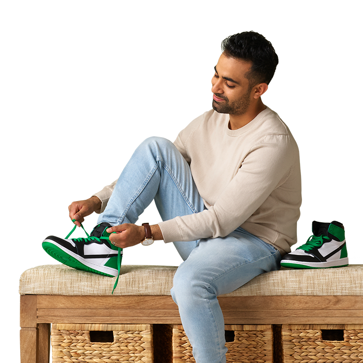 adult South Asian male sitting on a hallway bench tying is green and white sneakers
