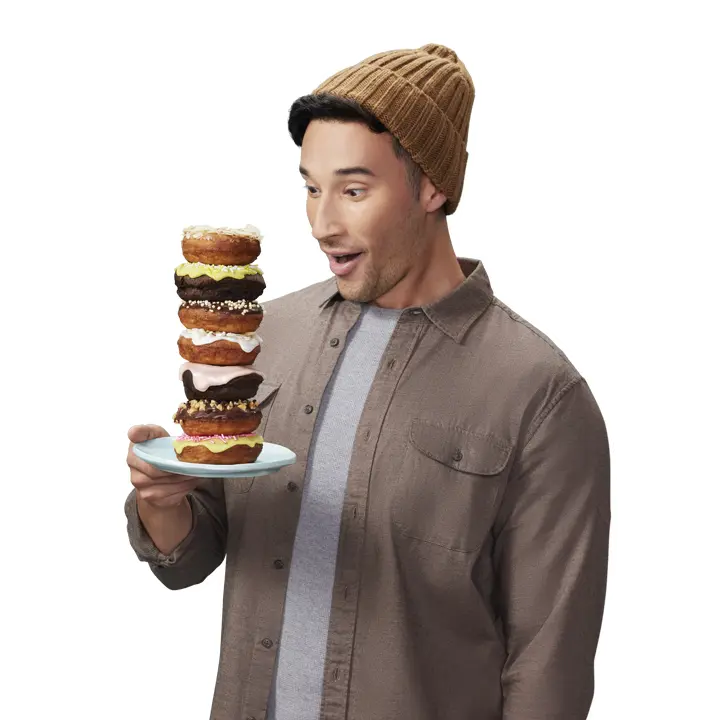 young man smiling at a plate stacked high with donuts