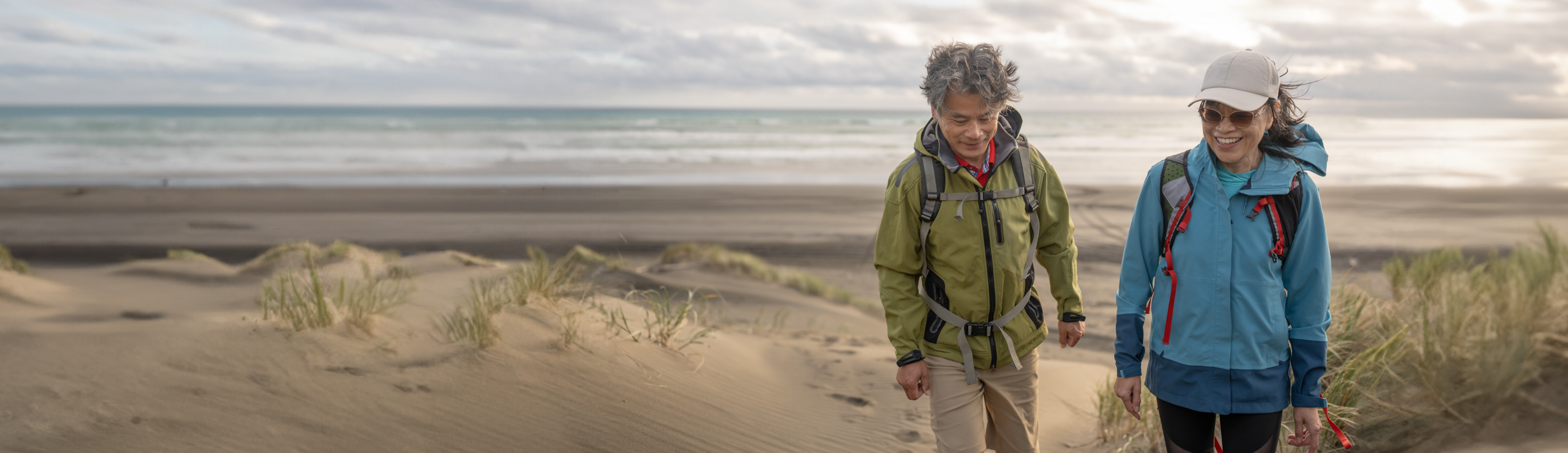 couple with wind breaker coats walking on beach