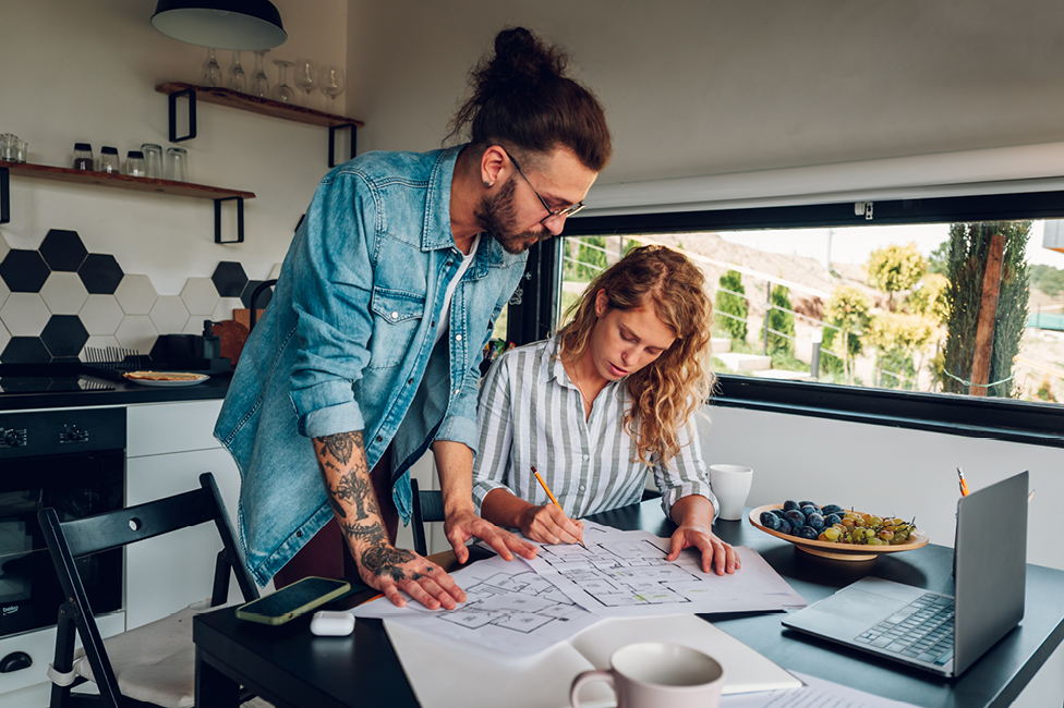 A  young man and woman reviewing floor plans over a desk in the kitchen