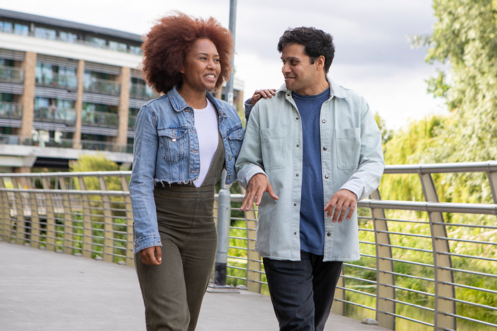 Smiling man and woman walking across a small bridge over a pond