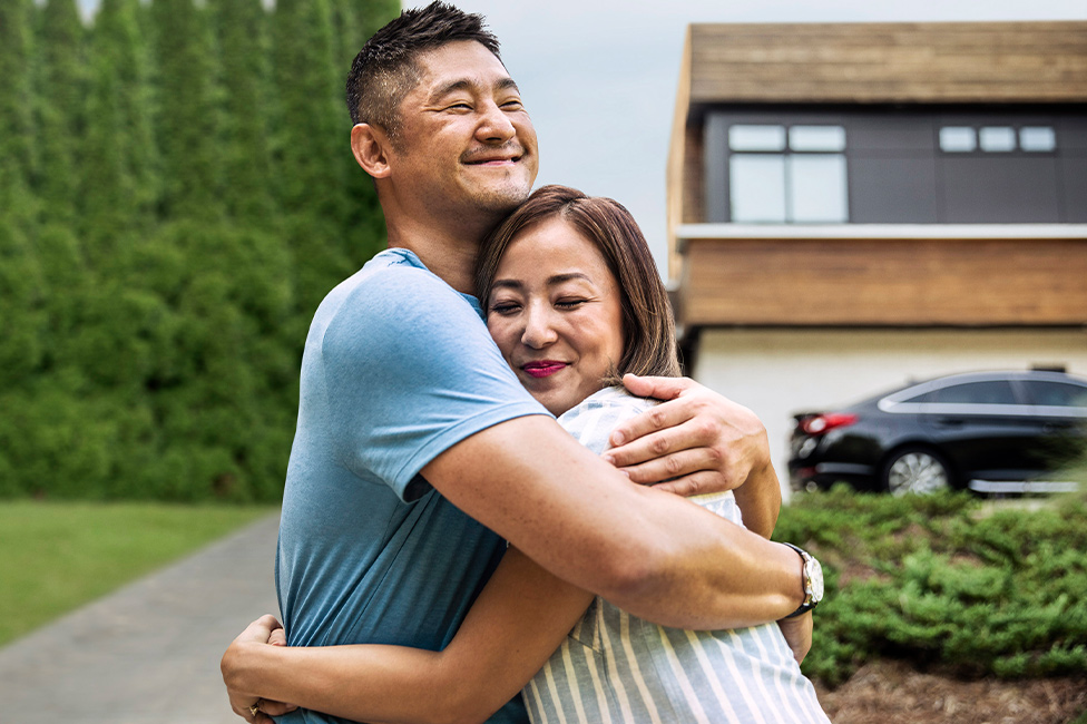 husband and wife hugging in front of a house