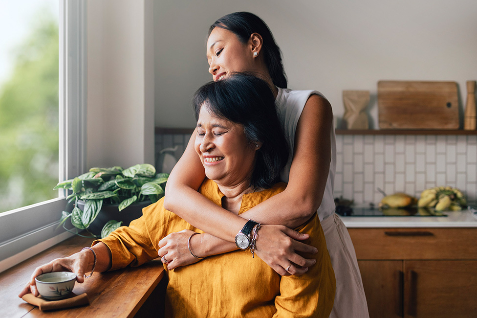 daughter hugging her mom both looking out the window of their home