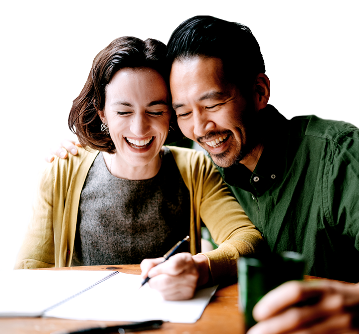 husband and wife laughing and sitting at a table with an open notebook