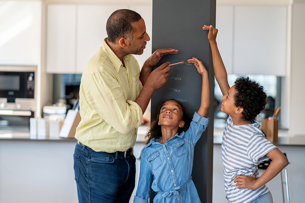 dad marking the height of his young daughter and son on the pillar in their kitchen