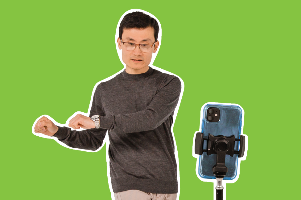 middle aged Asian man recording himself dancing with a smartphone on a tripod
