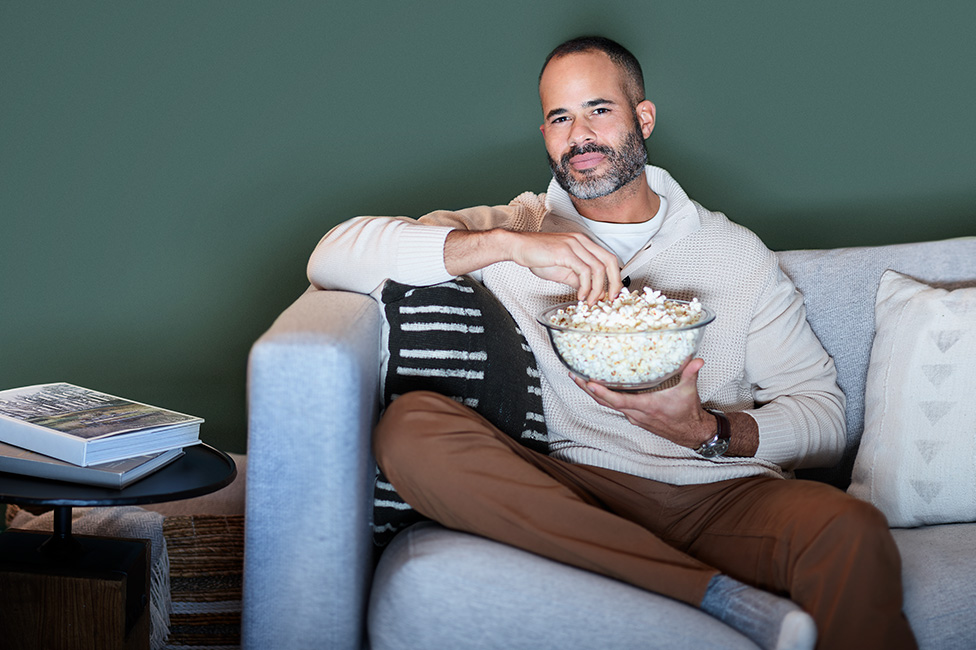 young man sitting on his couch watching TV holding a bowl of popcorn