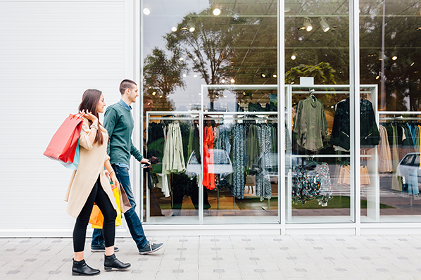 young couple walking in front of a clothing store window with shopping bags