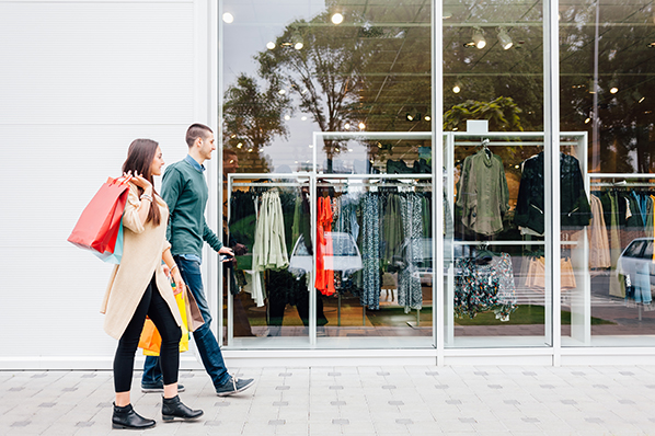 young couple walking in front of the clothing store window with shopping bags