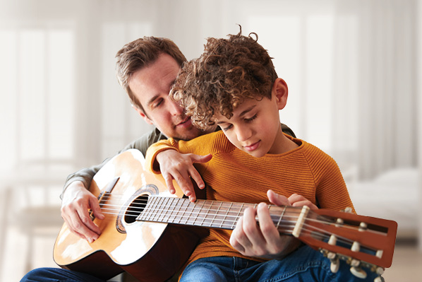dad teaching boy how to play the guitar