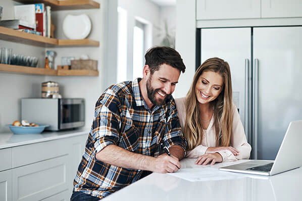 young couple sitting at the kitchen counter chatting and looking at papers and their laptop