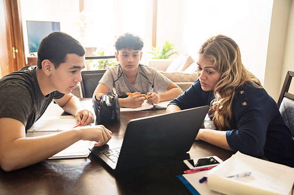a mom showing her two teenage sons how to budget on the family computer